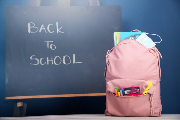 Backpack with school supplies and medical mask. COVID-19 prevention while going back to school and new normal concept. - Foto, Imagem