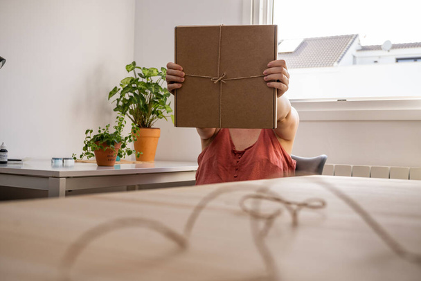 young girl opening a handmade eco-friendly gift wrapped in a cardboard box in her home - Foto, Bild