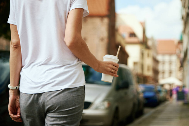 Kubek z papieru do kawy w rękach kobiety. Kobieta pije kawę, żeby iść na ulicę.. - Zdjęcie, obraz