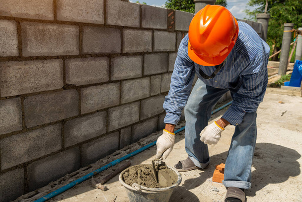 Працівник кладки робить бетонну стіну цементним блоком і штукатуркою на будівельному майданчику
. - Фото, зображення
