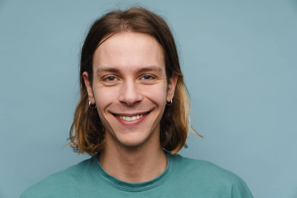 Young white man wearing t-shirt smiling and looking at camera isolated over blue wall - 写真・画像