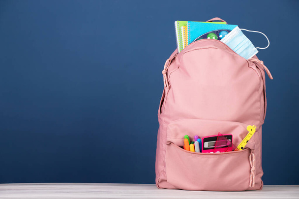 Backpack with school supplies and medical mask. COVID-19 prevention while going back to school and new normal concept. - Photo, image