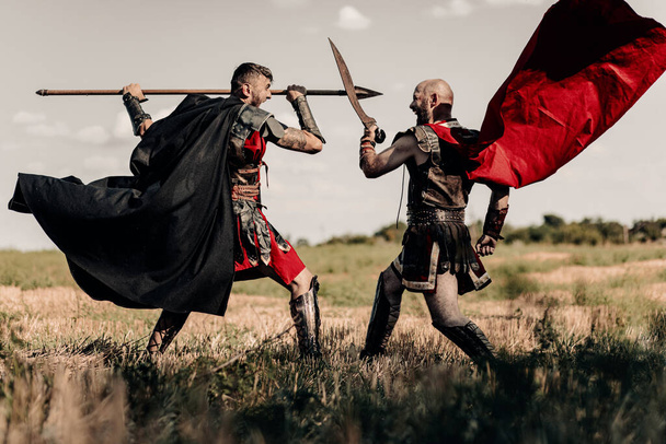 Bataille avec lance et épée entre deux anciens guerriers grecs ou romains en tenue de combat et manteaux sur prairie. - Photo, image