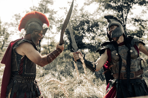 Bitva s meči mezi dvěma starověkými řeckými nebo římskými bojovníky v bojových šatech a pláštích na louce. - Fotografie, Obrázek