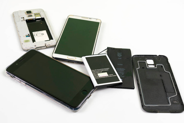 Zepsuty stary smartfon i stara bateria na białym tle. - Zdjęcie, obraz