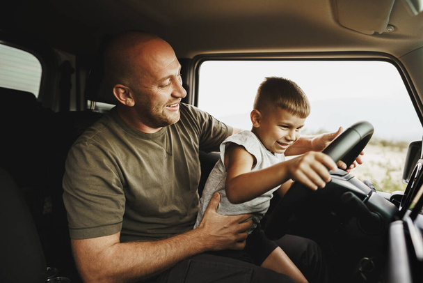 Father teaches little son to drive on road trip - Foto, afbeelding