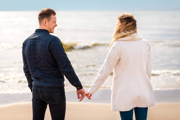 Jovem casal apaixonado, homem e mulher atraentes desfrutando de noite romântica na praia, de mãos dadas assistindo o pôr do sol - Foto, Imagem