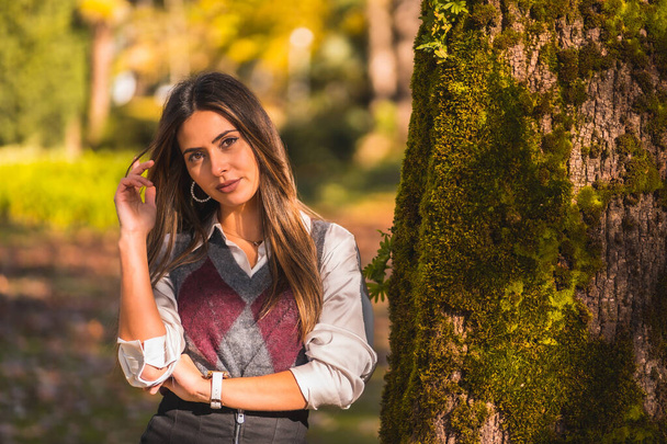 A young Caucasian brunette, in a park next to a tree one autumn afternoon - Photo, image