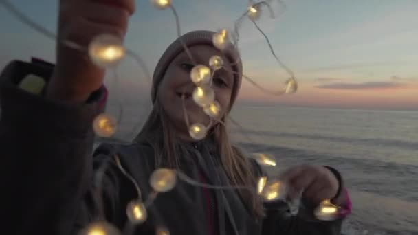 Dziewczyna na plaży gospodarstwa świecące światła girlanda - Materiał filmowy, wideo