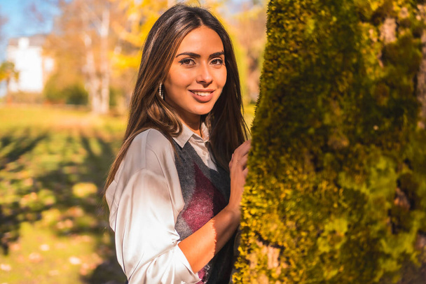 Une jeune fille de collège brune caucasienne, dans un parc à côté d'un arbre un après-midi d'automne - Photo, image