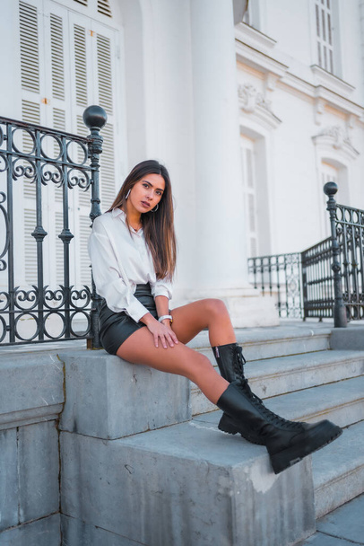 Lifestyle, fashionable pose of a young brunette in a black leather skirt and shirt sitting on some stairs - Foto, immagini