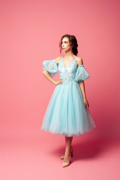 full-length portrait of elegant young woman in blue evening dress with full skirt and lantern sleeves, isolated on pink background - Фото, изображение