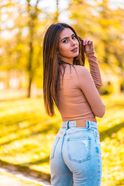 Lifestyle, portrait of a young Caucasian brunette in a pink sweater and jeans walking in a park in autumn - Foto, Imagen