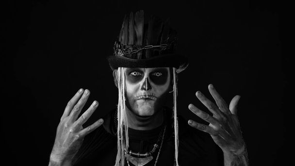 Przerażający mężczyzna z okropnym halloween szkieletowym makijażem robi miny, chowa się za ręką - Zdjęcie, obraz