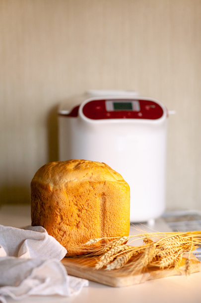 Хлеб от хлебопечки с пшеничными шипами на доске с кухонной салфеткой. - Фото, изображение