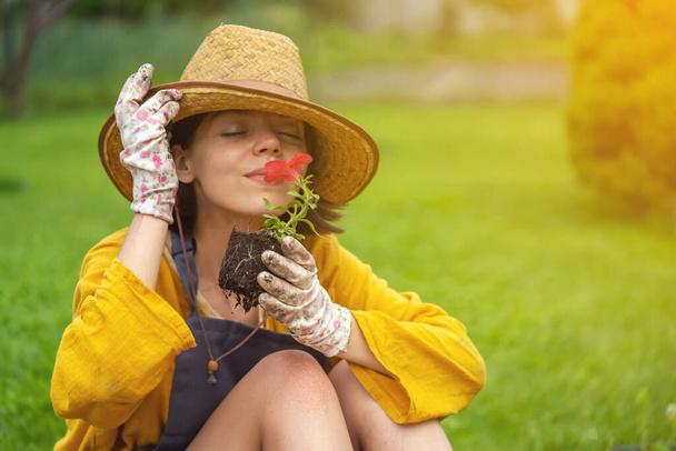 Une jeune femme jardinière tient une fleur de pétunia dans un pot de tourbe - Photo, image