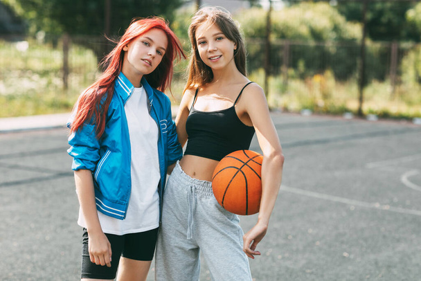 Portrait de deux charmantes filles avec un ballon de basket sur le terrain de sport. Amitié, meilleurs amis, sport - Photo, image