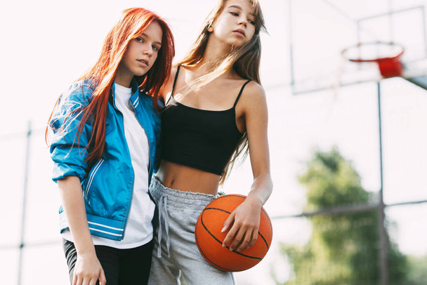 Πορτρέτο δύο γοητευτικών κοριτσιών με μπάσκετ στο γήπεδο. Φιλία, κολλητοί, αθλήματα - Φωτογραφία, εικόνα