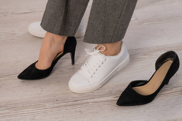 Close-up business woman takes off her shoes puts on white leather sneakers. - Foto, Bild