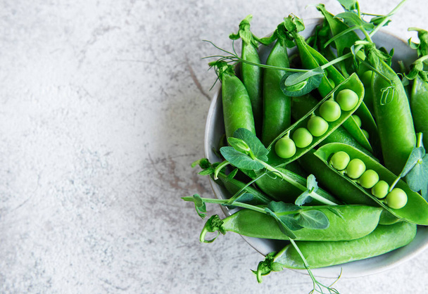 コンクリートの背景にもやしと新鮮な緑のエンドウ豆のポッドと緑のエンドウ豆。健康的な食事、新鮮な野菜の概念 - 写真・画像