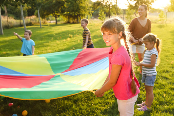 Group of children and teachers playing with rainbow playground parachute on green grass. Summer camp activity - Photo, image