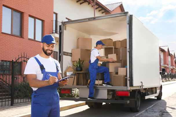 Moving service workers outdoors, unloading boxes and checking list - Foto, imagen