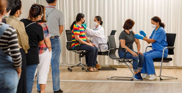 Çeşitli yaşlarda vatandaşlar sıraya dizilip aşı yapılmasını beklerken sağlık görevlileri de maskeli yaşlı kadınlara iğne yapıyor. Covid-19 veya Coronavirus sürü bağışıklık kavramı. - Fotoğraf, Görsel