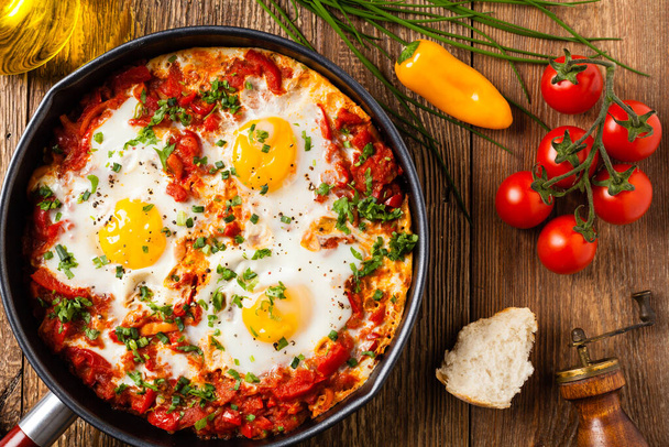 Shakshouka, dish of eggs poached in a sauce of tomatoes, chili peppers, onions. Top view.  - Фото, изображение