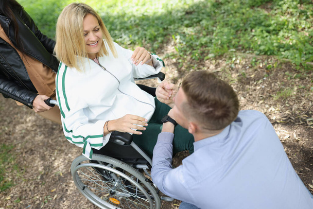 Mężczyzna komunikuje się z uśmiechniętą niepełnosprawną kobietą na krześle w parku - Zdjęcie, obraz