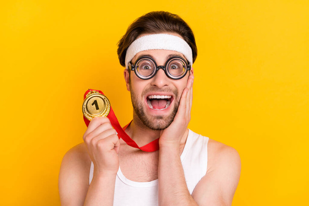 Portrait of handsome cheerful guy nerd leader holding golden medal great success isolated over bright yellow color background - Фото, зображення