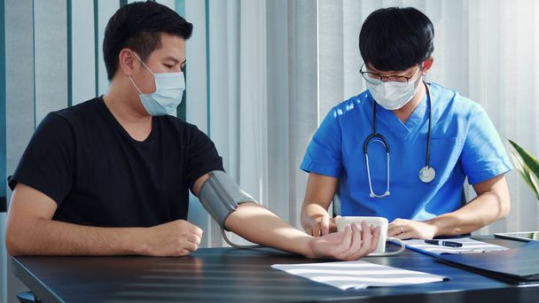 Asiatischer Arzt verwendet das Blutdruckmessgerät eines Patienten zum Zeitpunkt seiner jährlichen Untersuchung und erklärt seinen Blutdruck. - Foto, Bild