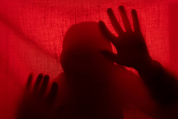 赤い光のカーテンの後ろに男のシルエット。ハロウィンと暴力の概念 - 写真・画像