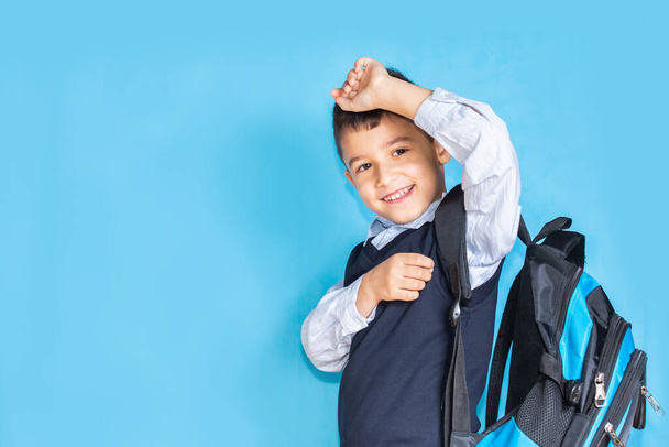 happy first-grader boy with a school satchel on his back on a blue background - 写真・画像