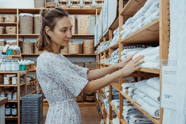 Young woman choosing natural stylish textiles for her apartment in a modern home furniture and home decor store. Pleasant time for shopping in the offline store. - Zdjęcie, obraz