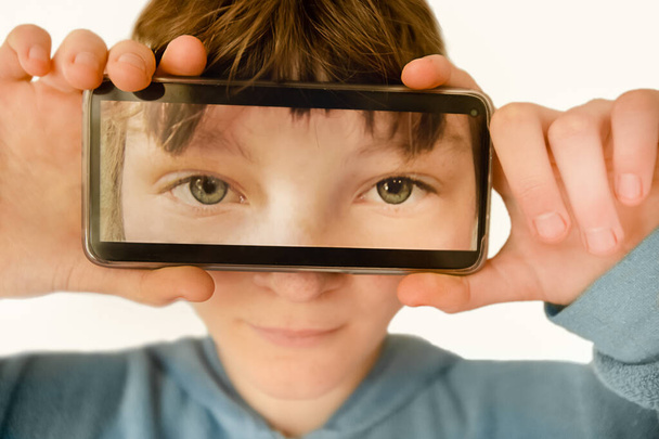 Αστείο πορτρέτο του κοριτσιού που κρατά κινητό τηλέφωνο μπροστά από το πρόσωπό της, κινητή τεχνολογία, φωτογραφία smartphone - Φωτογραφία, εικόνα