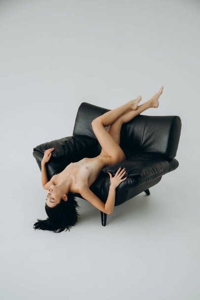 Γυμνή, όμορφη μελαχρινή κοπέλα σε γυμνό φωτογραφικό πρόγραμμα σε φωτογραφείο, ποζάροντας σε πολυθρόνα και κάτω από το ντους - Φωτογραφία, εικόνα