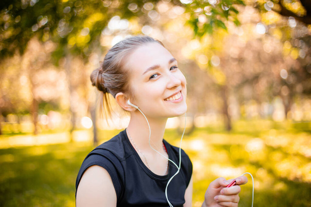 Young sportive woman sits in the park and listens to music on headphones. - Фото, зображення