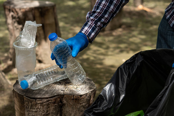 Jongeman haalt vuilnisflessen op Plastic in het park om het milieu schoon te maken - Foto, afbeelding