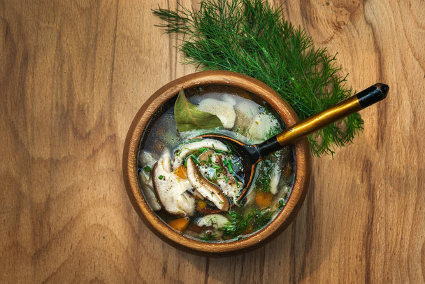 Zupa grzybowa Porcini z ziemniakami, marchewką, cebulą i kilkoma ziołami w drewnianym talerzu - Zdjęcie, obraz