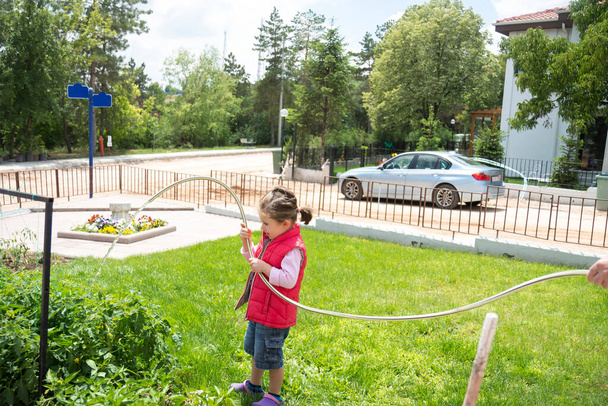 Κοριτσάκι ποτίζει σπορόφυτα ντομάτας και πιπεριού στον κήπο του με λάστιχο κήπου. επιλεκτική εστίαση. - Φωτογραφία, εικόνα