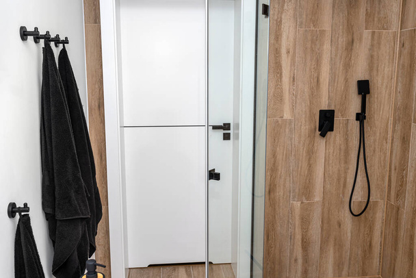 Uma moderna casa de banho com uma porta de chuveiro aberta, forrada com azulejos de cerâmica imitando madeira. - Foto, Imagem
