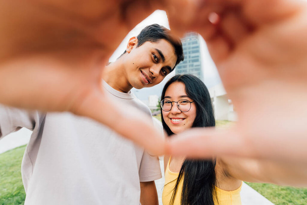 Genç Asyalı aşık çift dışarıda selfie çekiyor. Kalp el hareketi yapıyor. Gülümsüyor. - Fotoğraf, Görsel
