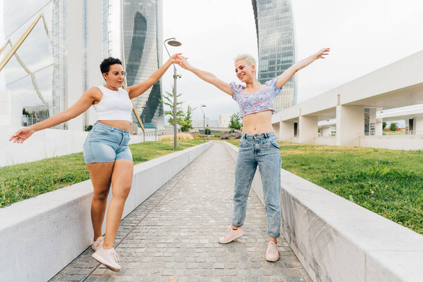 Дві багатоетнічні жінки друзі на відкритому повітрі відчувають себе вільними разом, спілкуючись весело танцюючи
 - Фото, зображення