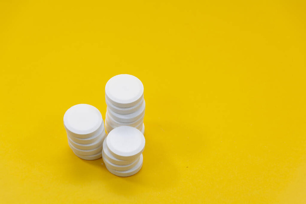 Trzy stosy białych tabletek leczniczych po lewej stronie żółtego tła - Zdjęcie, obraz
