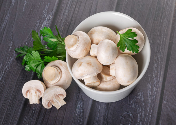 Young mushrooms in a white bowl with fresh parsley leaves on a dark wooden background - Фото, изображение