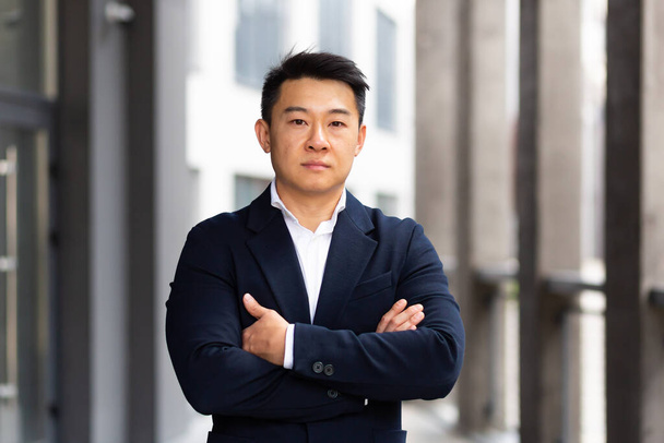 portrait of a serious asian in a business suit looking at the camera with arms crossed - Фото, изображение