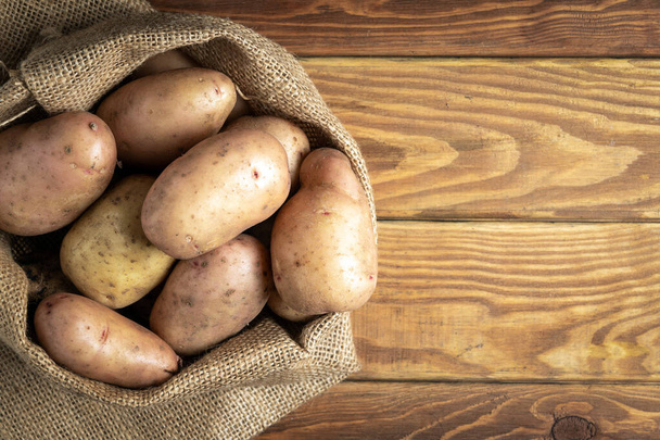 Saco de batatas após a colheita em tábuas de madeira vintage. Batata orgânica para cozinhar. Espaço publicitário gratuito - Foto, Imagem