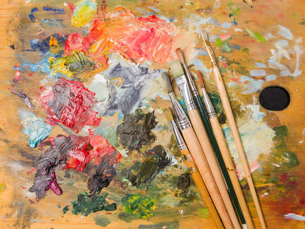 Artist's palette. Oil art paints extruded onto a wooden palette. Tubes and brushes lie on a colorful board - Φωτογραφία, εικόνα