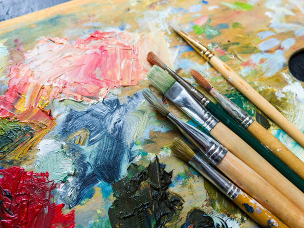 Artist's palette. Oil art paints extruded onto a wooden palette. Tubes and brushes lie on a colorful board - 写真・画像
