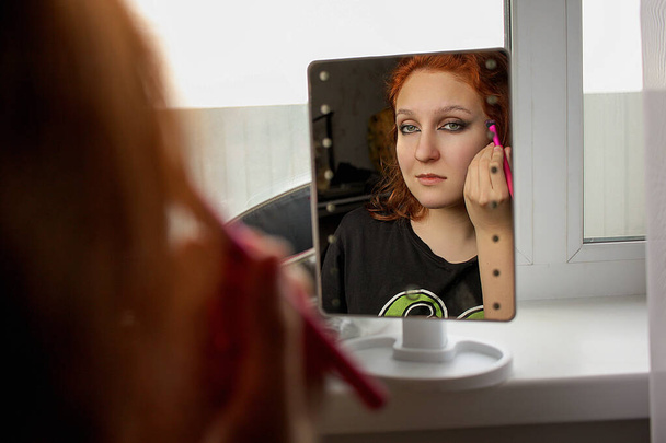 Fiatal nő alkalmazó smink néz a tükörbe - Fotó, kép